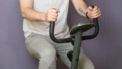 A close-up view of a mans hands gripping the handlebars of a stationary exercise bike. He is wearing a white t-shirt and his focus is intense as he pedals for a good workout.