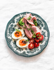 Delicious breakfast, snack - boiled egg, cherry tomatoes, cucumber and ham sandwich on a light background, top view