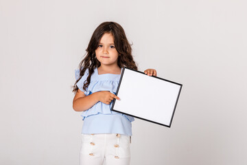 White banner. Little child girl model in summer blue and white cloth on white background hold white blank paper. Young smiling girl show blank board.