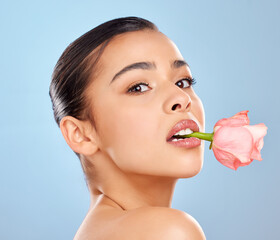 Woman, portrait and rose skincare in studio, mouth and sustainable cosmetics on blue background. Female person, plant and organic facial treatment, pink dermatology and flower for eco friendly makeup