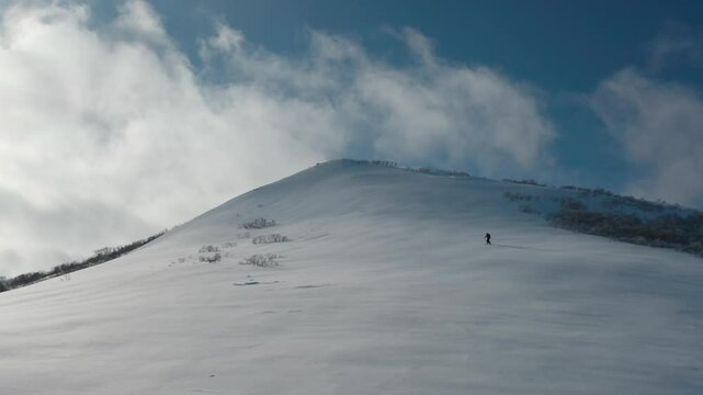 Snowboarder on snowy Iwanai mountain in Japan under a blue sky with clouds
