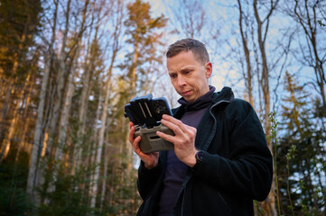 Close up view of drone operator holding remote controller in the mountains. Traveler controlling a drone flying over mountains with remote control. Shooting aerial videography and photography.