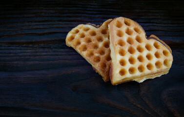 Two heart-shaped Viennese waffles lie on a dark wooden board.