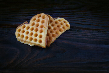 Two heart-shaped Viennese waffles lie on a dark wooden board.