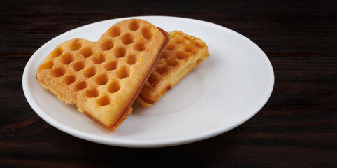 Two Viennese waffles lie on a white plate. Viennese waffles in the shape of a heart.