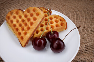 Viennese waffles with cherries lie on a white plate. Viennese waffles in the shape of a heart.