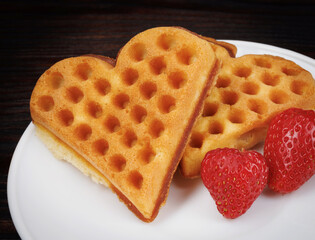 Viennese waffles with strawberries lie on a white plate. Viennese waffles in the shape of a heart.
