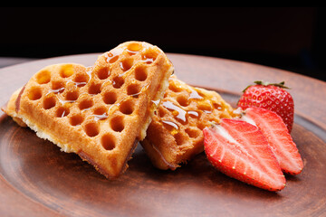 Viennese waffles drizzled with honey in the shape of a heart lie on a clay plate. Viennese waffles with cut strawberries.