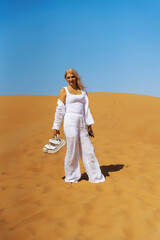 Woman in stylish white shirt and pants happy to explore Rub al Khali Desert sand dunes in United Arab Emirates.