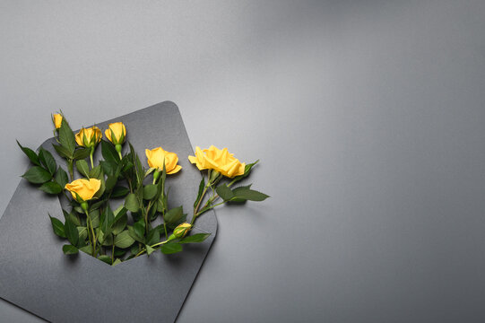 Invitation or greeting card mockup with gray envelope with small yellow roses on gray background.