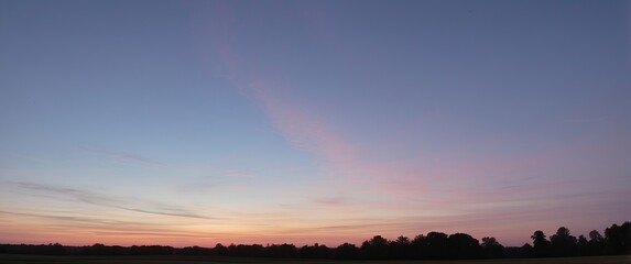 A tranquil evening with a serene sunset painting the sky in pink and blue hues, silhouetting the distant tree line and creating a peaceful landscape