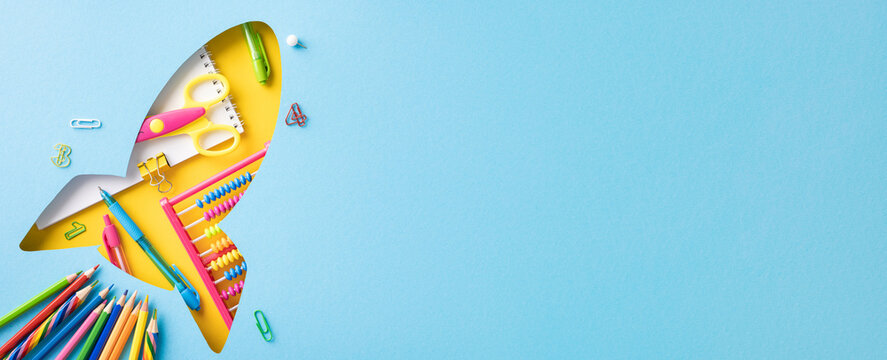 Top view of school supplies arranged in a rocket shape on blue background, symbolizing creativity and back to school
