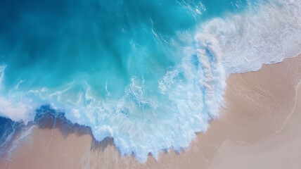 Aerial view of ocean waves crashing on the beach, creating a dramatic and dynamic scene. The blue water reflects sunlight as it surges against sandy shore.