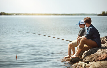 Happy dad, son and fishing with rod on rock by lake, ocean or beach together in nature. Father with kid, young child or little boy for bonding, teaching tips or lesson to catch by sea water or coast © Reese Coop/peopleimages.com
