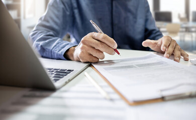 Asian businessman using laptop working online to review document report at office. legal expert, professional lawyer reading and checking business report or insurance contract before sign