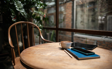 Comfortable workplace on wooden table by the window  in cafe with tablet, coffee drink and mobile phone put on note book, vintage background