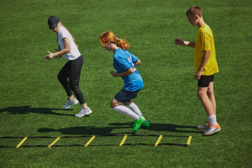 Athletic Training on Field Kids wearing sports gear engaged in challenging footwork exercise with agility ladder equipment. Concept of sport, school, childhood, hobby, active lifestyle