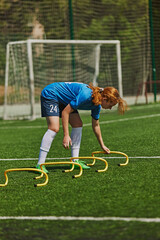 Focused Athletic Training. Young female athlete in blue jersey training with agility drills on sunny soccer field. Focus and skills. Concept of sport, school, childhood, hobby, active lifestyle