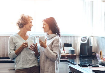 Morning, coffee and mother with daughter in kitchen for conversation, talking and enjoy beverage together. Family, home and mature mom with happy woman with drink for bonding, relationship and love