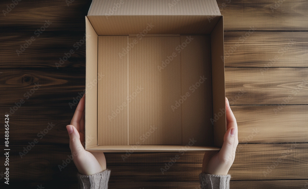 Poster hands holding an open empty cardboard box on a wooden surface.