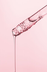 close-up of a serum oil pipette with a falling drop on a pink background
