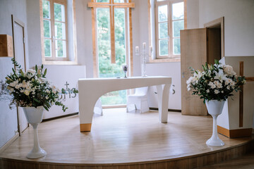 Valmiera, Latvia - September 9, 2023 - A church altar decorated with white flowers and candles, with large windows and a wooden cross, creating a serene and sacred atmosphere.