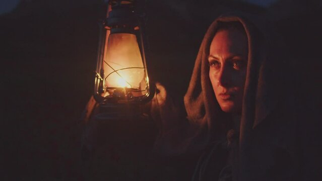 Portrait of a woman in vintage clothes with a kerosene lamp in her raised hand in the dark making signs with light
