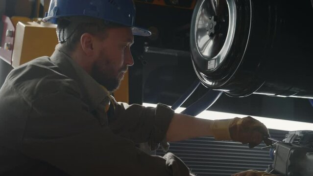 Male mechanic in hardhat and workwear fixing machine part with screwdriver while working in industrial plant