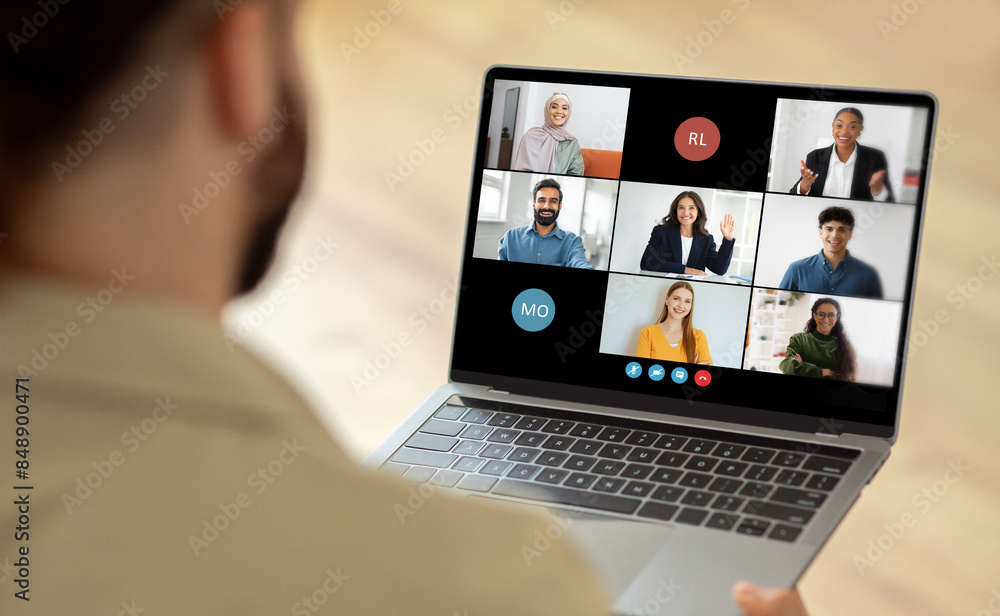 Poster Man using a laptop while a group of people are visible on the screen. The person is engaged in virtual communication or collaboration with the individuals displayed on the laptop screen.