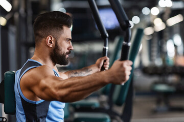 A man with a beard is working out on a chest press machine at the gym. He is focused on his workout...