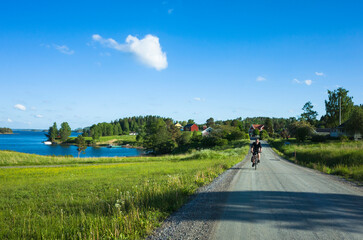 Swedish countryside landscape, Adult man cycling on a gravel road from village by the lake on a warm summer day, Lake Foxen and Väng village in Värmland, Sweden