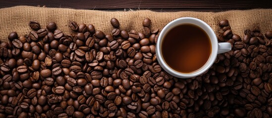 Naklejka premium Top view of a cup of coffee arranged beautifully among carefully selected Arabica coffee beans on a table napkin providing a pleasing and artistic copy space image