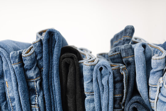 A stack of folded jeans in various shades of blue and black on a white background.