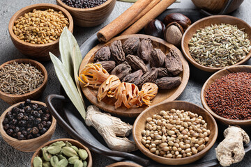 A variety of whole textured Indian spices in wooden bowls on a gray background close-up
