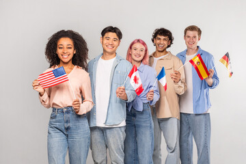 Multiethnic group of young adults stand together holding flags of different countries. They are all...