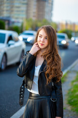 A young smiling girl in a good mood walks around the city. Teenage girl, portrait against the background of houses and roads. Fashionable youth style trend.