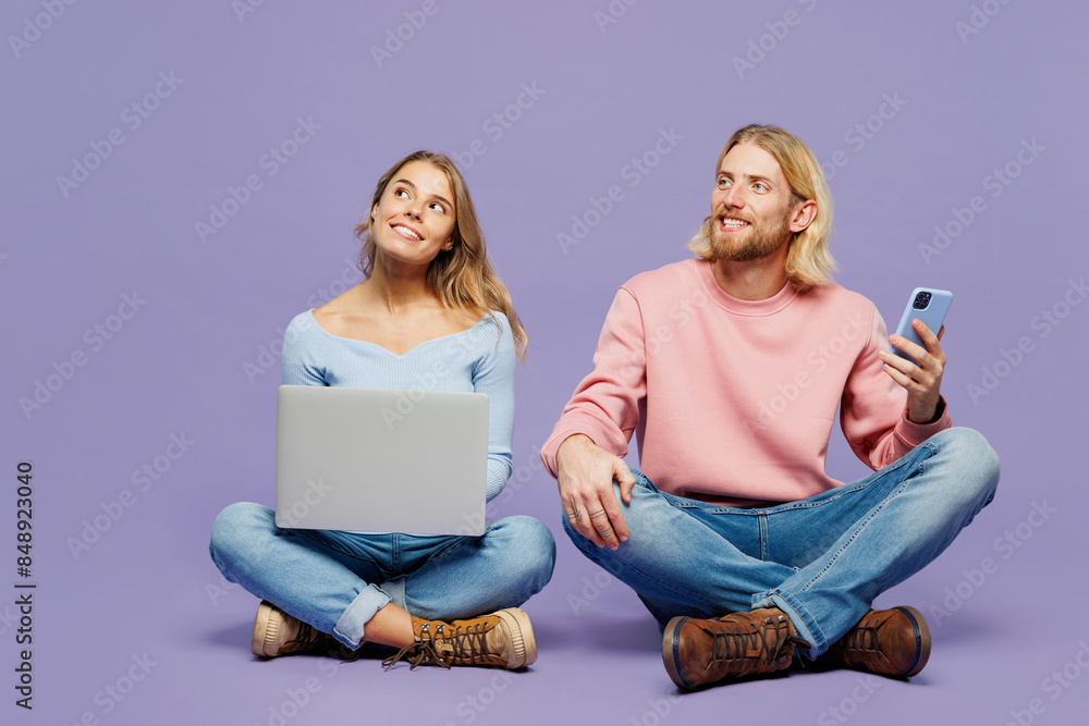 Wall mural Full body young couple two friends family IT man woman wear pink blue casual clothes together sitting use mobile cell phone work on laptop pc computer look aside isolated on plain purple background.