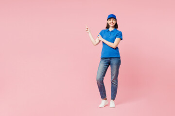 Full body happy delivery girl employee woman wear blue cap t-shirt uniform workwear work as dealer courier point index finger aside on area isolated on plain pastel pink background. Service concept.