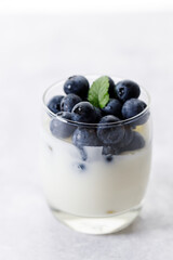 Ripe organic blueberries with yogurt in a glass on white stone table background. Selective focus.