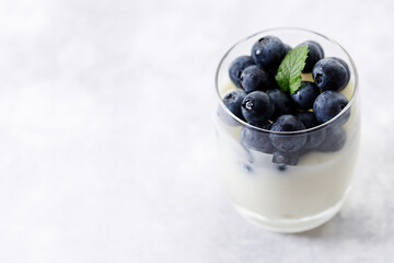 Ripe organic blueberries with yogurt in a glass on white stone table background. Selective focus.