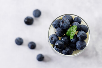 Ripe organic blueberries with yogurt in a glass on white stone table background. Selective focus.