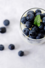Ripe organic blueberries with yogurt in a glass on white stone table background. Selective focus.