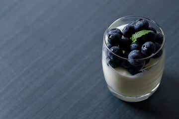 Ripe organic blueberries with yogurt in a glass on black stone table background. Selective focus.