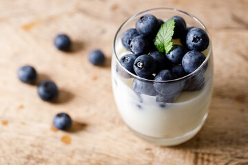 Ripe organic blueberries with yogurt in a glass on rustic wooden table background. Selective focus.