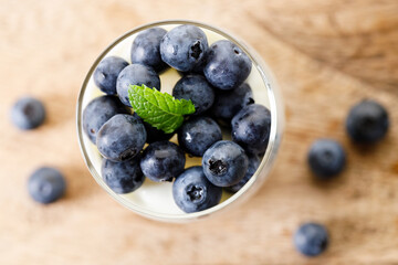 Ripe organic blueberries with yogurt in a glass on rustic wooden table background. Selective focus.