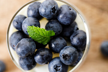 Ripe organic blueberries with yogurt in a glass on rustic wooden table background. Selective focus.