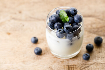 Ripe organic blueberries with yogurt in a glass on rustic wooden table background. Selective focus.