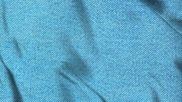 Close-up of chemical wash blue denim fabric texture with visible diagonal weave pattern and slight wrinkles, gently blowing in the wind. 4K Motion Graphics.