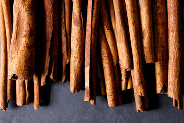 Cinnamon sticks dried tree bark spice on black stone table background. Selective focus.