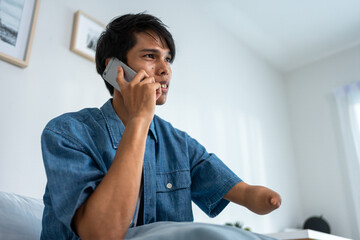 Asian young amputee without arm talk on mobile phone in living room. 